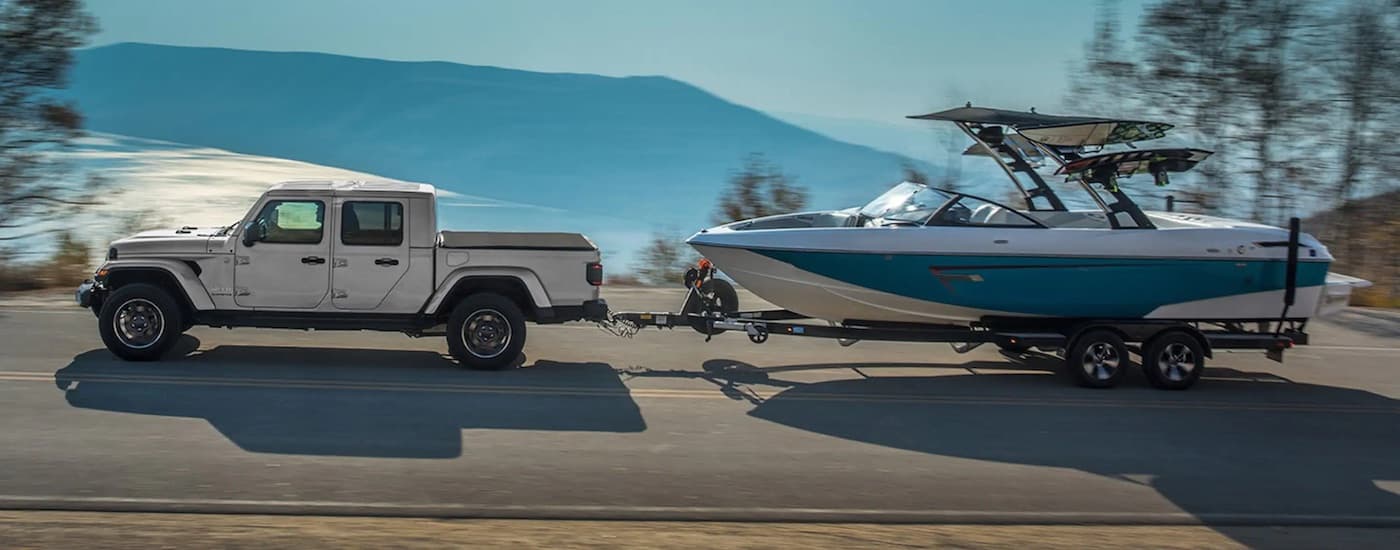 A silver 2023 Jeep Gladiator is shown from the side while towing a boat after leaving a used Jeep dealer.
