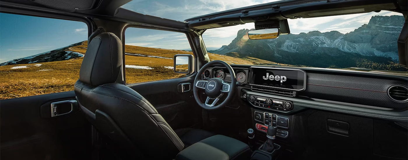 The black interior of a 2024 Jeep Wrangler for sale is shown from the back seats.