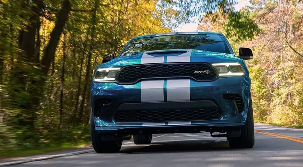 A blue 2024 Dodge Durango SRT Hellcat is shown driving on a tree-lined road.