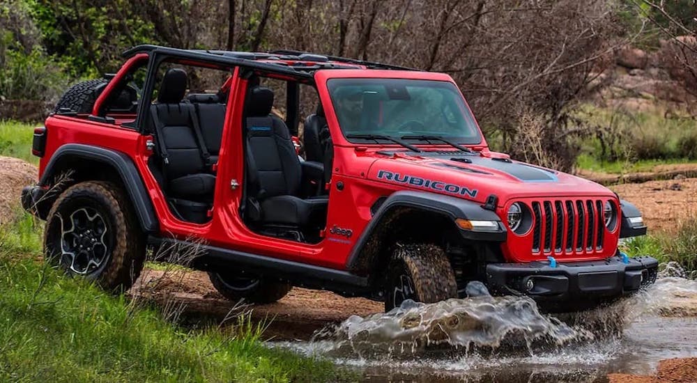 A red 2023 Jeep Wrangler Rubicon 4xe is shown from the side while off-roading.