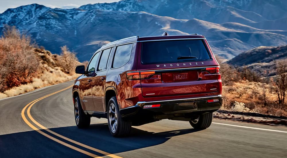 Rear view of a red 2024 Jeep Wagoneer driving on a mountain road.
