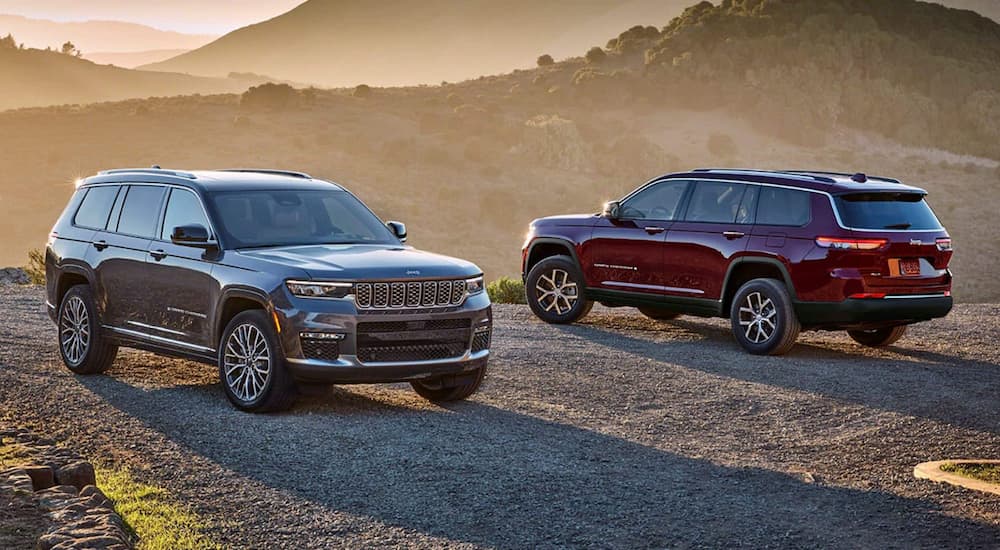 A grey 2024 Jeep Grand Cherokee Summit and a red Grand Cherokee Limited parked at sunset.