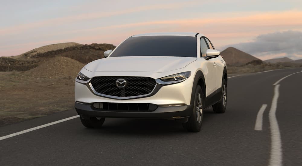 A white 2021 Mazda CX-30 driving from a dealer with used cars for sale.