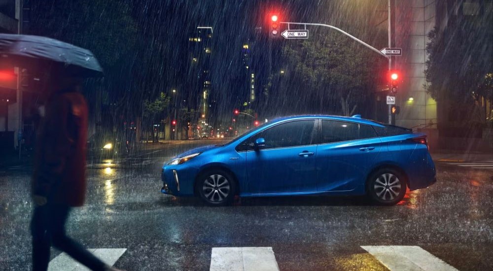 Side angle view of a blue 2021 Toyota Prius driving in a rainy city.