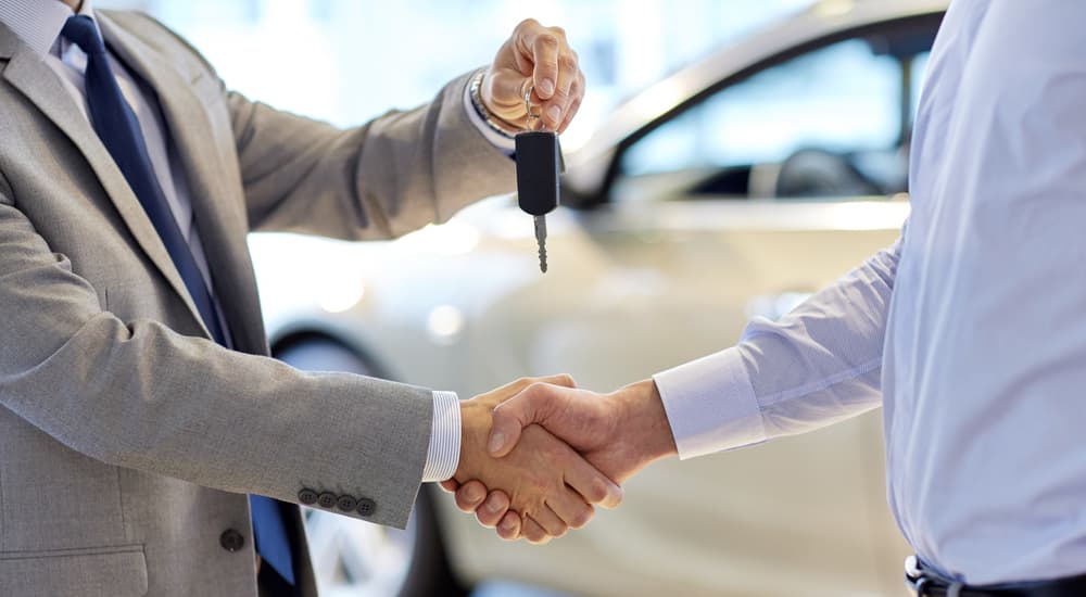 Two men shaking hands at a dealership while one offers a key fob.