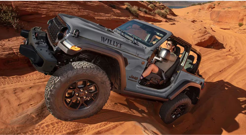 A silver 2025 Jeep Wrangler Willys climbing up a sand dune.