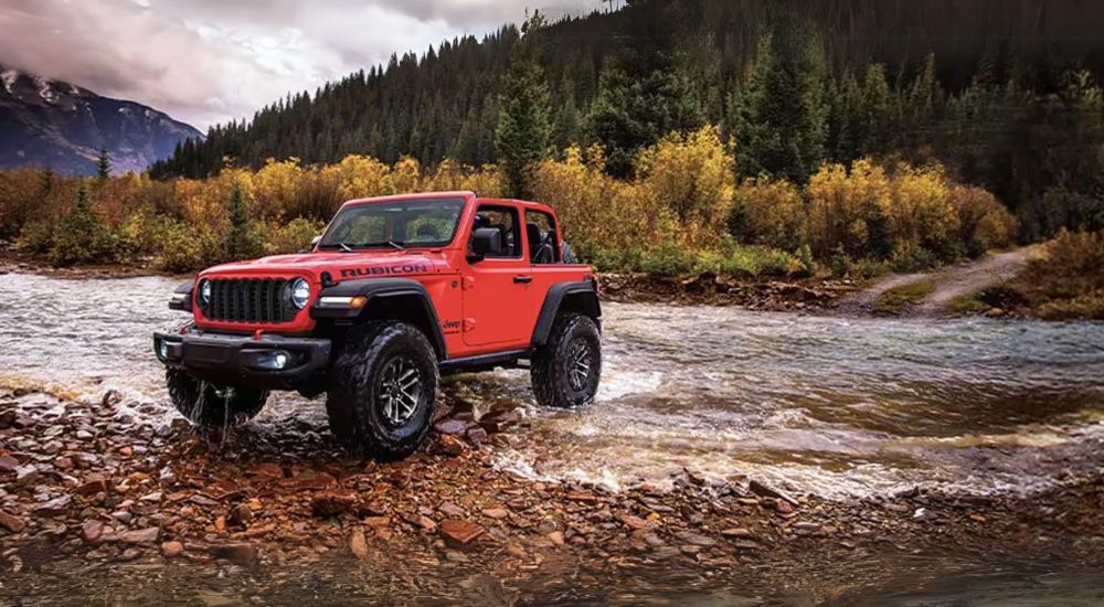 A red 2024 Jeep Wrangler Rubicon parked near a stream