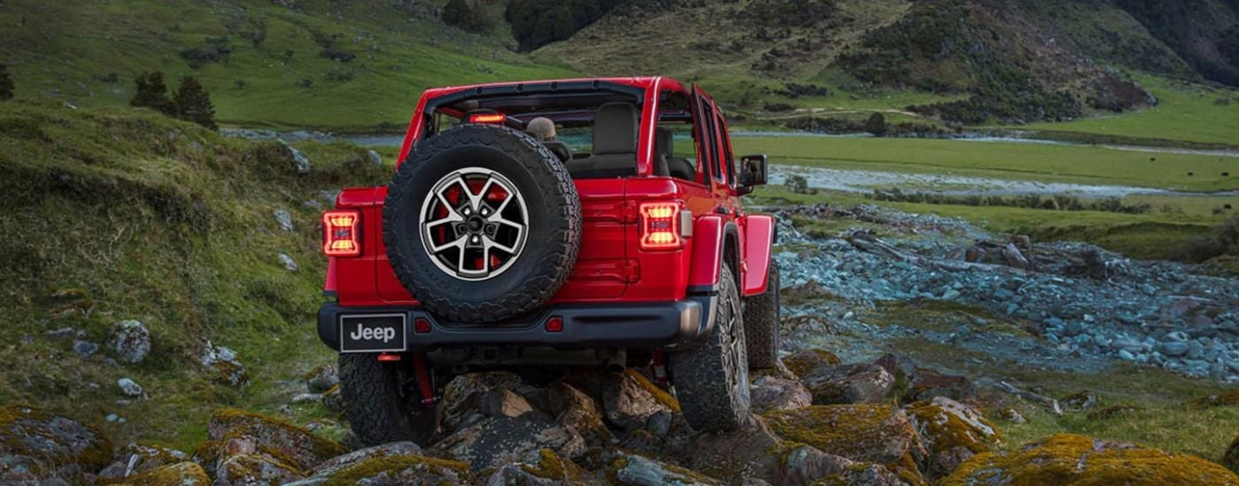 Rear view of a red 2024 Jeep Wrangler Unlimited driving over rocky terrain.
