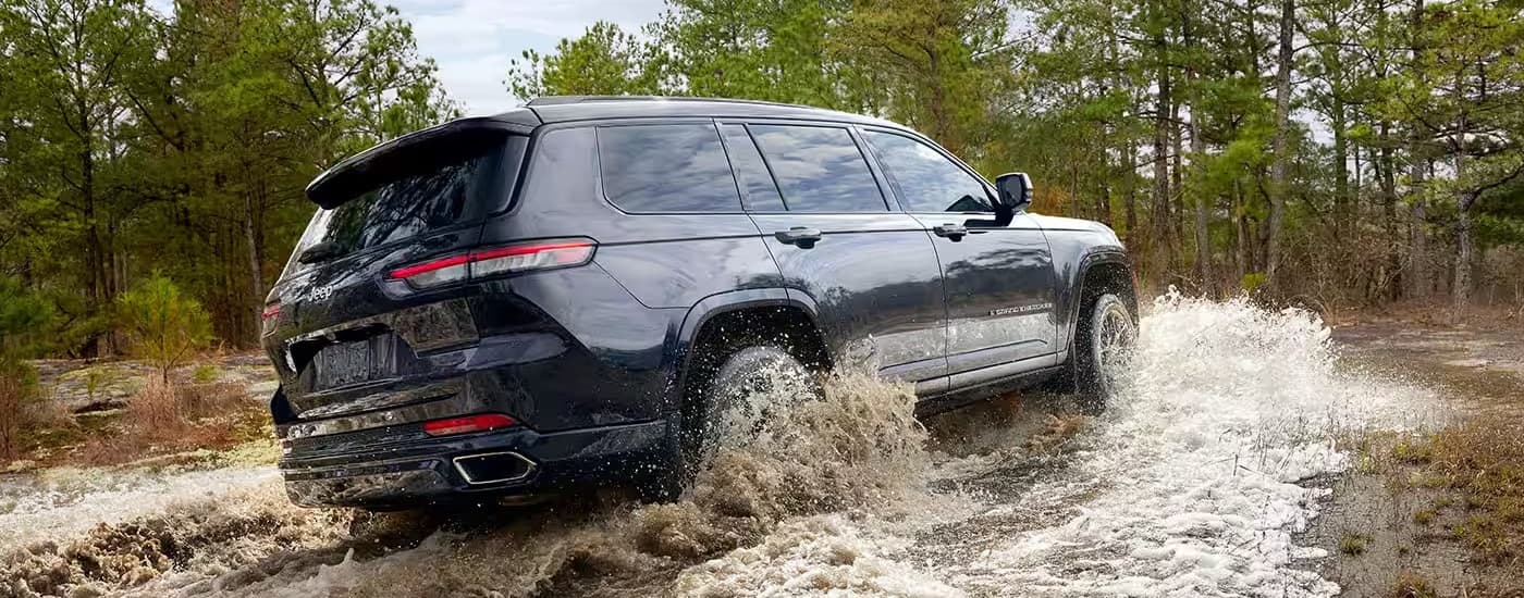 A black 2024 Jeep Grand Cherokee is shown from the rear at an angle while driving through mud after leaving a Jeep dealer near Morton.