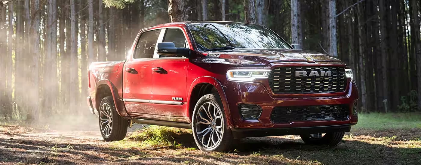 A red 2025 Ram 1500 Tungsten is parked on a grassy trail in the woods after leaving a Ram dealer.