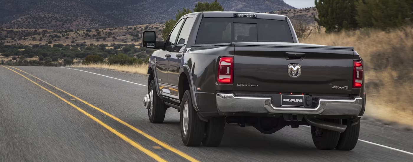 Rear view of a black 2024 Ram 3500 Limited driving down an open road.